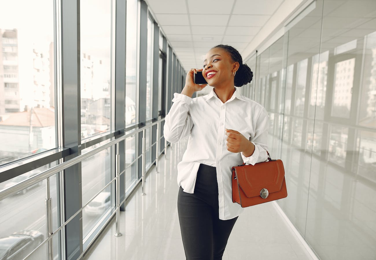 A Black woman stands in an office building hallway talking on the phone