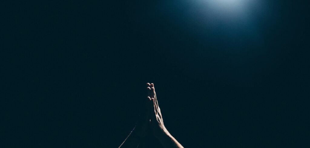 Praying hands surrounded by a dark background